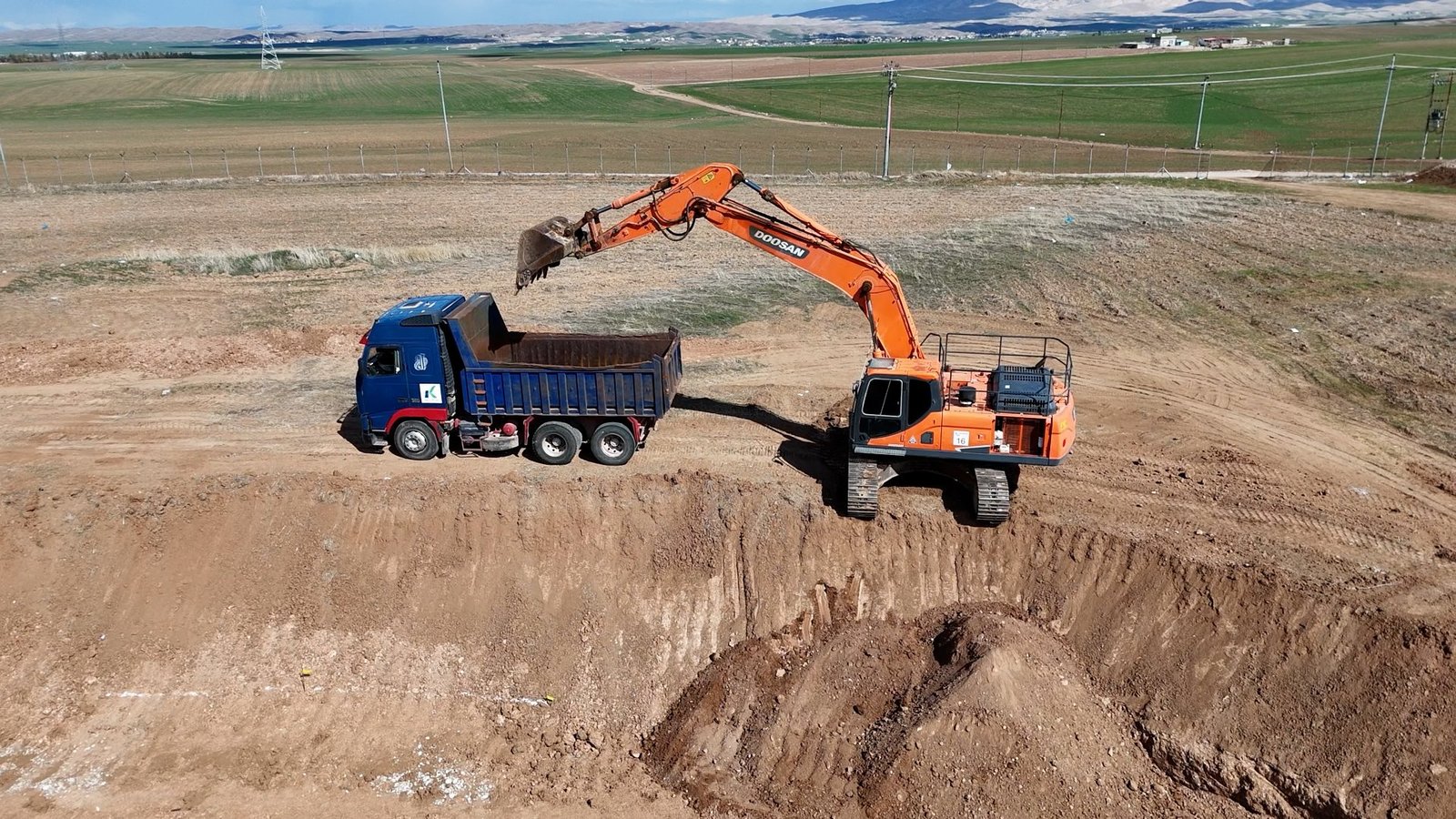 An excavator loading a KATO truck beside an excavation