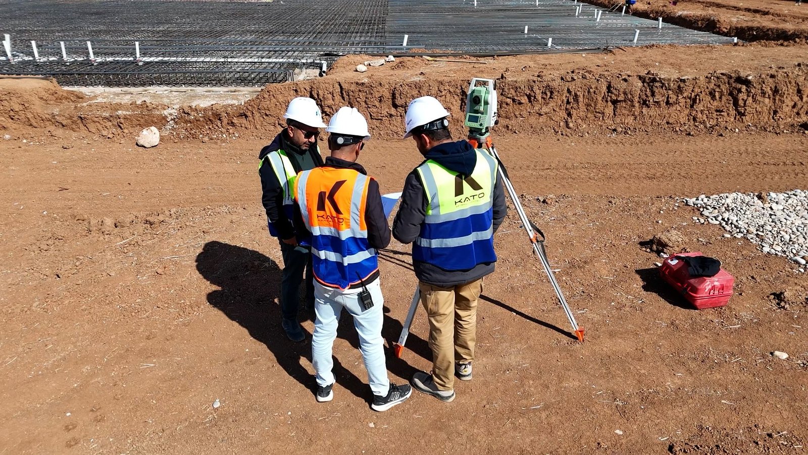 KATO personnel reviewing plans with surveying equipment beside them